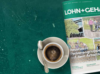 Eine Tasse Kaffee neben einer Zeitschrift über persönliches Management und Personalwesen auf einer strukturierten grünen Oberfläche.