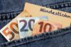 Euro, die aus einer Jeanstasche hervorschauen, mit einem Zettel mit der Aufschrift „Mindestlohn“, was auf Deutsch „Mindestlohn“ bedeutet und für Personalmanagement relevant ist.