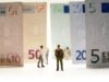 Zwischen übergroßen Euro-Banknoten platzierte kleine Figuren schaffen eine Szene, die mit Perspektive und Maßstab spielt.