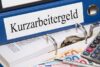 Finanzen verwalten mit Kurzarbeitergeld: Unterlagen und Rechner auf dem Schreibtisch.