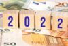 Holzklötze mit den Zahlen „2022“ stehen auf einem Hintergrund aus Euro-Banknoten.