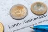Euro-Münzen auf einer deutschen Lohn-/Gehaltsabrechnung mit einem Stift, der auf Finanzplanung oder Gehaltsberechnung hinweist.
