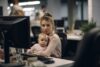 Eine berufstätige Frau, die im Büro Multitasking betreibt, während sie ihr entzückendes Baby hält, was die moderne Balance von Karriere und Elternschaft in dynamischen Humanressourcen widerspiegelt.