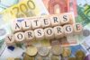 Holzklötze mit der Aufschrift „Altersvorsorge“ auf einem Hintergrund aus verschiedenen Euro-Banknoten und -Münzen symbolisieren im deutschsprachigen Kontext die Altersvorsorge oder Altersvorsorge.