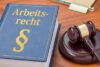 Ein Buch mit dem Titel „Arbeitsrecht“ neben einem Hammer auf einer Holzoberfläche, das die Rechtsgewalt und die Entscheidung arbeitsbezogener Rechtsangelegenheiten symbolisiert.