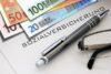 Ein Finanzplanungskonzept mit Euro-Banknoten, einem Stift, einer Brille und einem Dokument mit der Aufschrift „Sozialversicherung“, was auf Englisch „Sozialversicherung“ bedeutet.
