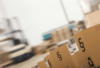 Eine verschwommene Ansicht eines geschäftigen Lagers, wobei der Fokus auf einer Reihe von Kartons mit Barcodes und Nummern liegt, die auf den Prozess der Bestandsverwaltung und Logistik hinweisen.