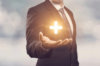 Eine Person in Geschäftskleidung hält ein leuchtendes Kreuzsymbol in der Handfläche, das den Glauben und die Spiritualität im Personalmanagement repräsentiert.
