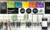 Die Teilnehmer drängen sich in einem modernen Konferenzsaal, in dem zahlreiche informative Banner für Keynote-Bühnen, Workshops und Networking-Zonen zu sehen sind.