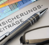 Eine Nahaufnahme eines Dokuments, auf dem das deutsche Wort „Versicherungsbeiträge“ steht, daneben ein Stift und eine Brille, was auf einen Rahmen für die Durchsicht von oder hindeutet