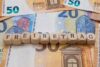 Holzwürfel mit der Aufschrift „Freibetrag“ auf einem Hintergrund aus Euro-Banknoten.