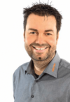 Ein lächelnder Mann mit Stoppeln, der ein graues Hemd mit Kragen vor weißem Hintergrund trägt und Personalmanagement repräsentiert.