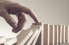 Eine menschliche Hand, die verhindert, dass eine Reihe Dominosteine umfällt, symbolisiert das Eingreifen oder das Stoppen einer Kettenreaktion im Personalmanagement.