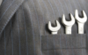 Ein markanter Kontrast zwischen Professionalität und Handarbeit: drei Metallschraubenschlüssel, ordentlich in der Tasche eines Nadelstreifenjacketts platziert.