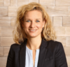 Professionelle Frau, spezialisiert auf Personalmanagement, mit freundlichem Lächeln posiert vor einer strukturierten Holzwand in Geschäftskleidung.