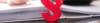 Ein rotes kaufmännisches Und-Symbol, das aufrecht auf einem Tisch steht, mit einem verschwommenen Hintergrund einer schreibenden Person und einem Stapel Dokumenten.