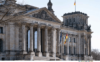 Majestätische neoklassizistische Architektur des Reichstagsgebäudes mit seinen ikonischen Säulen und Skulpturen unter einem klaren blauen Himmel, stolz unter der deutschen Flagge inmitten von Diskussionen über Personalmanagement und Humanress