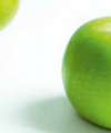Leuchtend grüne Limetten auf einer hellen Oberfläche, eine im Vordergrund scharf abgebildet, die andere leicht unscharf im Hintergrund, was Frische und ein pikantes Aroma suggeriert.