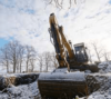 Ein ruhender Bagger an einem frostigen Wintertag, inmitten einer kargen Landschaft mit blattlosen Bäumen und einer dünnen Schneeschicht.