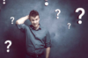 Mann kratzt sich mit verwirrtem Gesichtsausdruck am Kopf, umgeben von illustrierten Fragezeichen, die Verwirrung oder Unsicherheit symbolisieren.