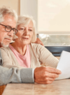 Ein älteres Ehepaar sitzt besorgt und aufmerksam an einem Tisch und geht gemeinsam Dokumente durch, möglicherweise über finanzielle, rechtliche oder gesundheitliche Angelegenheiten.