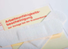 Ein Stück Papier mit dem Text „Arbeitsunfähigkeitsbescheinigung zur Vorlage bei der Krankenkasse“, teilweise mit einem Heftpflaster abgedeckt. Der Text ist auf Deutsch und weist typischerweise auf ein Dokument hin, das sich auf eine ärztliche Bescheinigung für die Krankenkasse bezieht.