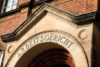 Blick auf den Eingang eines Backsteingebäudes mit einem großen Steintorbogen, in den das Wort „ARBEITSGERICHT“ eingraviert ist, was auf ein Arbeitsgericht in Deutschland hinweist. Der Torbogen ist ein markantes architektonisches Merkmal vor dem Hintergrund der roten Backsteinfassade.