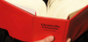 Eine Person hält ein offenes Buch mit einem leuchtend roten Einband in der Hand. Es trägt den Titel „Deutsche Gesetze Textsammlung“. Die Seiten sind dick und voller Text.
