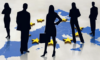 Silhouetten von zwei Frauen und drei Männern stehen auf einer Europakarte mit verstreuten gelben Sternen, die die Europäische Union anzeigen. Eine Frau hält eine Aktentasche, die Geschäft oder Führung symbolisiert. Sowohl die Männer als auch die Frauen tragen Geschäftskleidung.