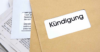 Ein Stapel Briefumschläge und eine aufgeschlagene Zeitung. Ein Umschlag hat ein sichtbares Fenster mit dem Wort „Kündigung“.