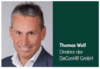 Eine Person mit kurzen grauen Haaren und hellem Teint trägt einen dunklen Anzug und ein weißes Hemd und lächelt vor einem hellgrauen Hintergrund. Neben der Person steht der Text „Thomas Wolf, Direktor der DeConHR GmbH“.