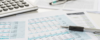 Ein mit Finanztabellen, einem Stift und einem Taschenrechner geschmückter Schreibtisch lässt auf eine sorgfältige Datenanalyse schließen. Zwischen den Zahlen und Diagrammen, die Feinheiten des Lohnsteuerrechts veranschaulichen, liegt nachdenklich eine Brille auf der Oberfläche.