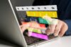 Digitale Darstellung eines Kalenders mit farblich markierten Wochen auf einem Laptopbildschirm, während eine Person mit einem Finger einen Termin auswählt – Symbolbild für digitale Arbeitszeiterfassung und moderne Arbeitszeitmodelle.