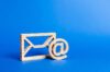 Symbolbild für personalisierte E-Mail-Adressen im Betriebsrat – Holzsymbole für Briefumschlag und @-Zeichen vor blauem Hintergrund, Thema Arbeitsrecht.