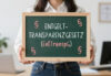 Frau hält Tafel mit Aufschrift "Entgelttransparenzgesetz (EntTranspG)" und Paragraphenzeichen – Symbol für Transparenzpflichten und Auskunftsansprüche im Arbeitsrecht